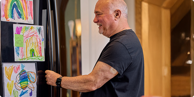 Dean smiling while looking at his grandchildren's drawings on the fridge