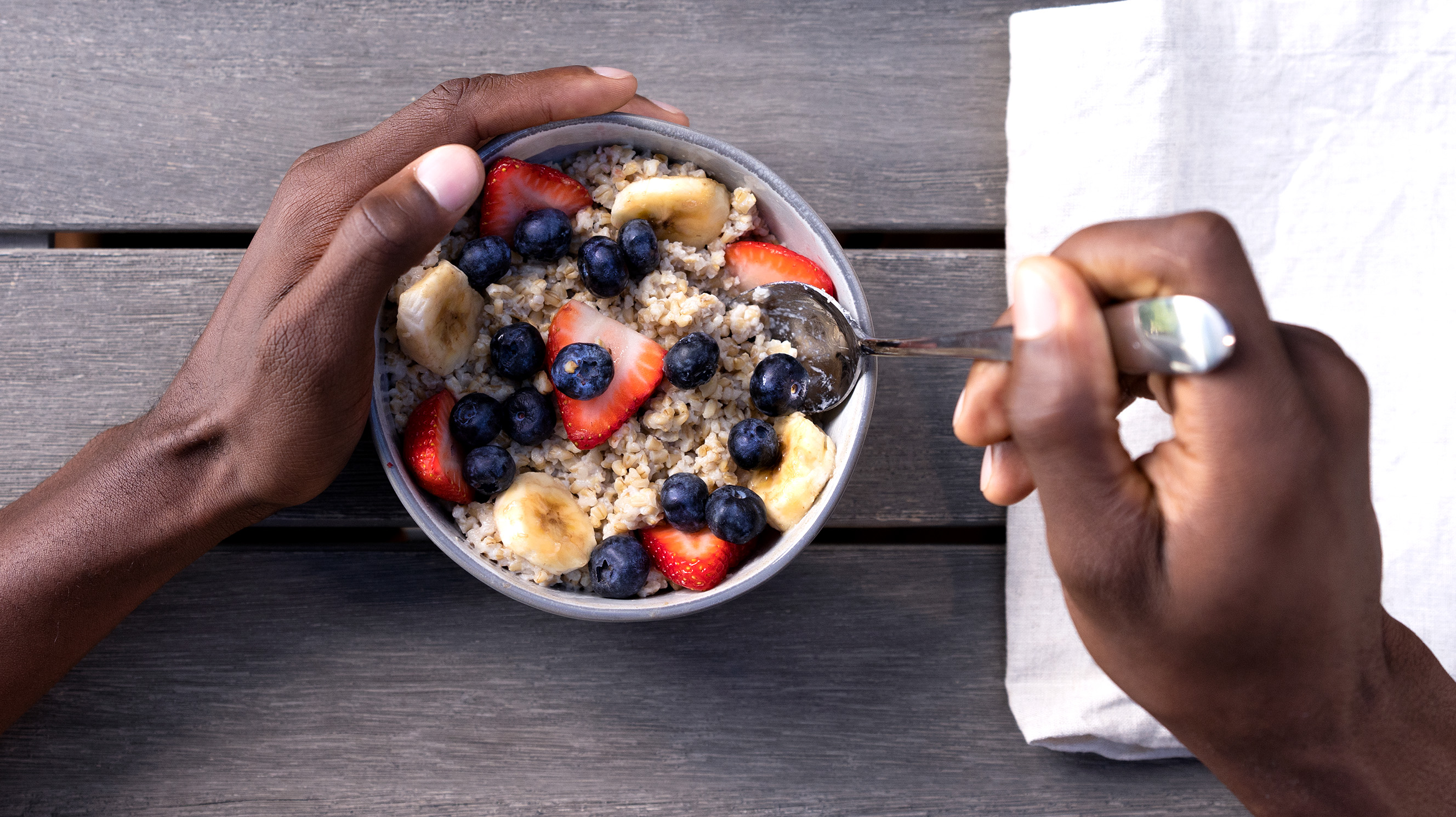 Hands holding a bowl of oatmeal and fruit with a spoon